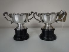 A pair of silver twin handled trophies, height 7.5 cm, on stands.
