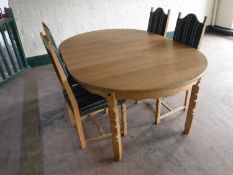 A circular blonde oak dining table with two leaves and four chairs