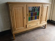 A blonde oak triple door sideboard with a stained panel glass door