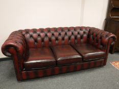 A three piece oxblood red leather Chesterfield suite comprising three seater settee,
