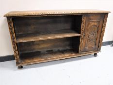 An early 20th century carved oak open low bookshelf fitted a cupboard