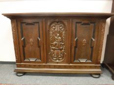 A heavily carved oak triple door sideboard on bun feet