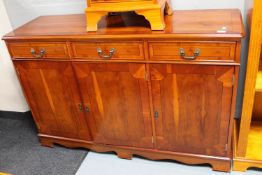 A reproduction yew wood three drawer sideboard