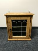 A blonde oak wall cabinet with leaded glass door