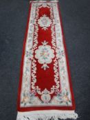 A Chinese fringed carpet runner on red ground,