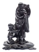 A Chinese black composition carved figure: of a beaded man with a shield and sword on his back,