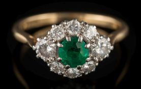 An emerald and diamond cluster ring: the central round emerald approximately 4.5mm diameter x 3.