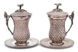 A pair of Egyptian silver mugs, covers and saucers: of waisted form,