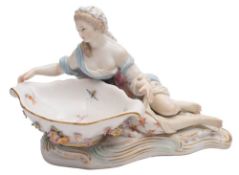 A Meissen figural sweetmeat dish: the shaped bowl applied with flowers and supported by a reclining