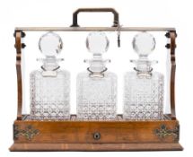 An Edwardian oak three decanter tantalus: the oak and silver plated frame with hinged fall front