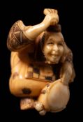 A Japanese carved ivory netsuke depicting a musician: beating a drum with his fan,