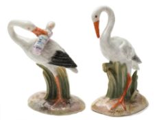 Two Meissen miniature models of storks: one holding a swaddled baby in its beak,