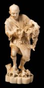 A Japanese carved ivory okimono of a grape gatherer: in traditional costume holding a basket of