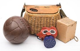 A wicker creel together with a brown leather football and a WWII childs gas mask.