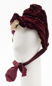A late Victorian purple velvet bonnet, with lace trim and ribbon ties.