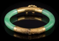 An early 20th century Chinese gold mounted green jade hinged bangle: with two hinged sections of