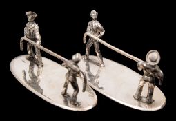 A pair of Edwardian silver plated knife rests of an army and navy tug o'war:,