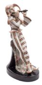A Goldscheider figure of a jester: playing a pipe and leaning against a column draped with a cloth,