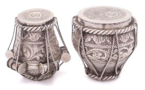 Two Indian white metal pots in the form of drums: having rope tied foliate and scroll decoration,