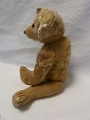 A large straw stuffed bear much of the plush worn off and stitched repairs, glass eyes with stitched