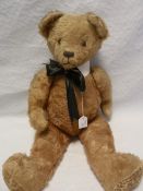 Large gold plush straw stuffed bear with glass eyes and a stitched nose and mouth with a white stiff