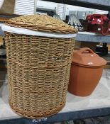 One wicker laundry basket containing a blue throw and large earthenware covered pot