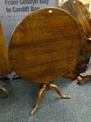 An antique oak circular tilt-top tea table on a turned column and tripod footed base, 88cms in