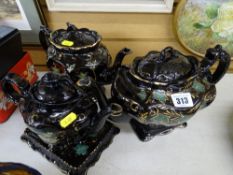 Three black lustre teapots, one on a small base tray