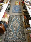 Two blue patterned rugs, a small mat with camels and riders and a rug pinned to a board