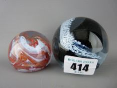 Two paperweights, one swirling cloud and snow and the other orange and white waves