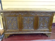 A REPRODUCTION CARVED OAK LIDDED BLANKET CHEST having leaf carved panels and decorative canted