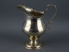 A HELMET SHAPED SILVER CREAM JUG on pedestal base with scroll handle, Chester 1920 (crease to the