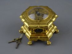 A GILT BRASS HORIZONTAL TABLE CLOCK of hexagonal form, raised on winged ball and claw feet with