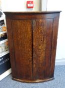 AN ANTIQUE OAK BOW FRONT TWO DOOR HANGING CORNER CUPBOARD, the doors with diamond shaped escutcheon,