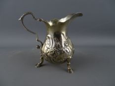 A GEORGE III SILVER CREAM JUG with floral embossed body and scroll handle on three hoof feet, London