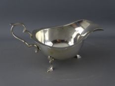 A HALLMARKED SILVER GRAVY/SAUCE BOAT with scroll handle on three hoofed feet, Birmingham 1921, 5.3
