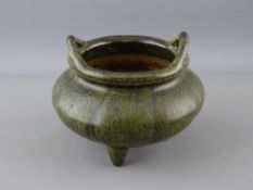 A CHINESE POTTERY TWIN HANDLED SENSOR raised on three feet with an all over mottled green glaze,