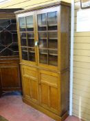 A SLIM GOLDEN OAK BOOKCASE CUPBOARD having twin upper glazed panel doors and base cupboard doors