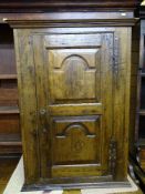 AN ANTIQUE JOINED OAK SINGLE DOOR WALL CUPBOARD, a twin shaped panelled door with iron 'H' hinges