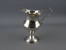 A GEORGE IV SILVER HELMET SHAPED PEDESTAL CREAM JUG with beaded foot and rim decoration, London
