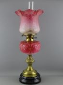 A VICTORIAN OIL LAMP with pink glass font and cranberry tinted shade on a baluster brass stem and