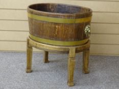 AN EARLY 20th CENTURY BRASS BOUND OAK WINE COOLER on stand with lion mask carry handles, 51 cms high