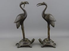 A PAIR OF ORIENTAL BRONZE STORKS riding on the backs of terrapins, 23 cms high (losses to the