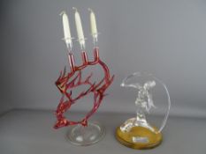 Stylized lady candelabra in cranberry glass and a clear glass example of Goddess Iris on a wooden