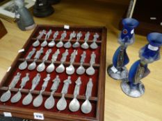 A rack displayed set of Canterbury Tales character spoons and a pair of fancy candlesticks Condition