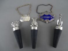 Three white metal bottle stoppers in the form of a seated teddy bear, an anchor and the sun, a white