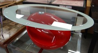 A contemporary coffee table of oval form with glass top and having red plastic base of abstract