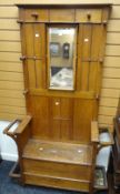A neat vintage oak hall stand with seat, side umbrella holders and centre swing mirror, also with