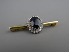 A NEAT SHORT NINE CARAT GOLD BAR BROOCH with large oval dark sapphire and surrounding small
