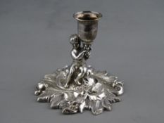 A SHORT STEMMED SILVER CANDLEHOLDER, the candle held aloft by a seated cherubic figurine on a base